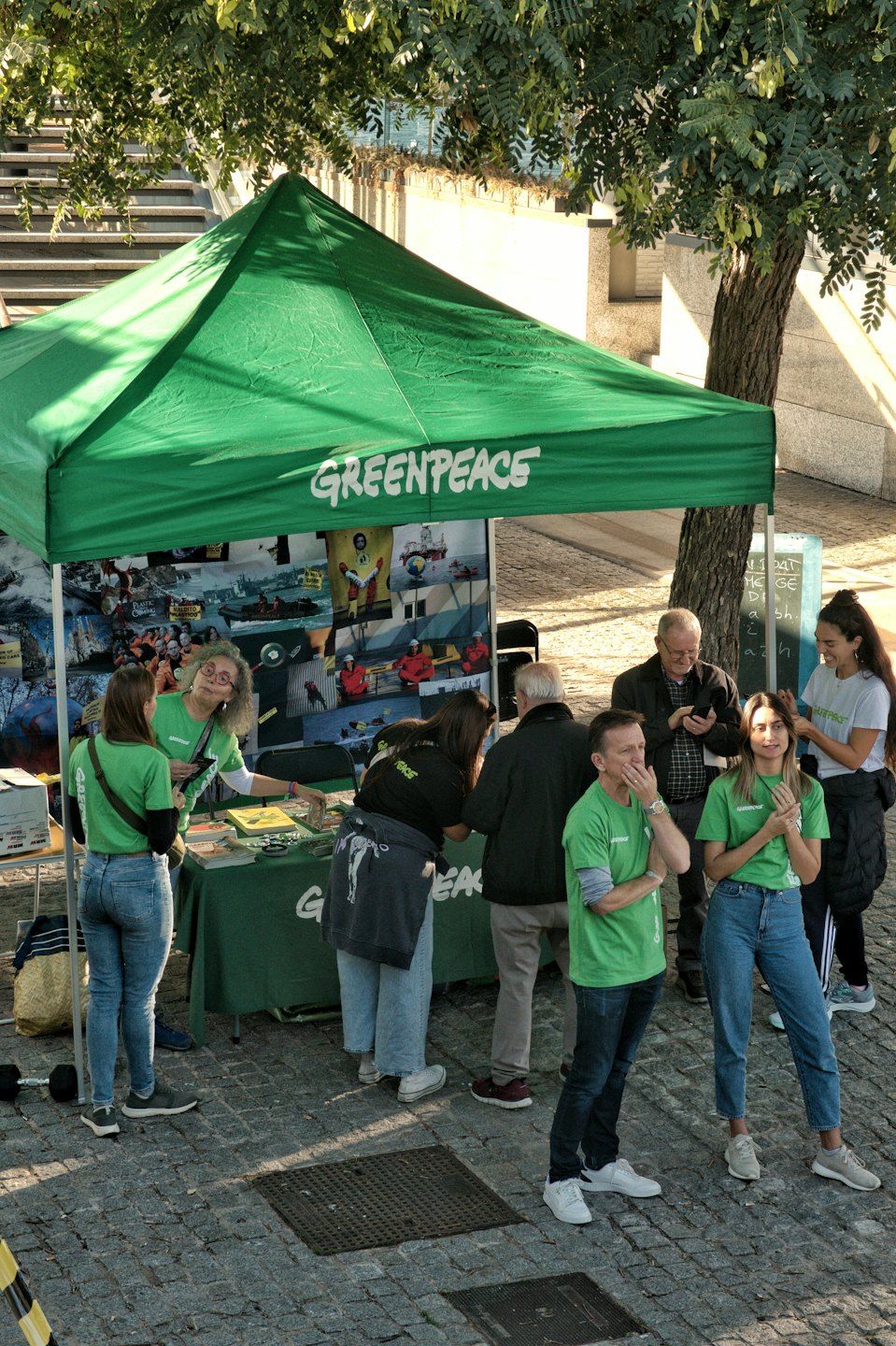 Volunteers stand at a green Greenpeace information booth outdoors.